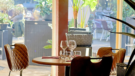L'Effet Jardin Lattes : table dressée avec verres à vin et fauteuils en cuir, près des baies vitrées donnant sur le patio végétalisé.