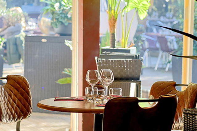 L'Effet Jardin Lattes : table dressée avec verres à vin et fauteuils en cuir, près des baies vitrées donnant sur le patio végétalisé.